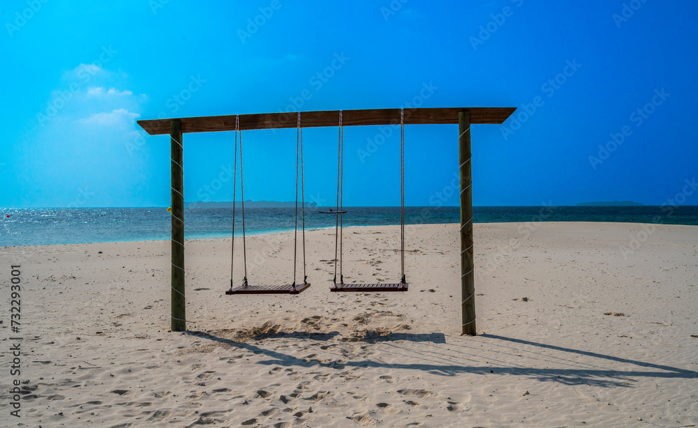 Double wooden swing on the sandy beach with an ocean view. Sunny weather.