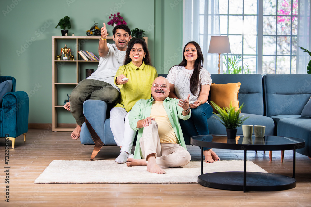 Indian family of four sitting on couch watching TV, operating with remote control Indian family of four sitting on couch watching TV, operating with remote control