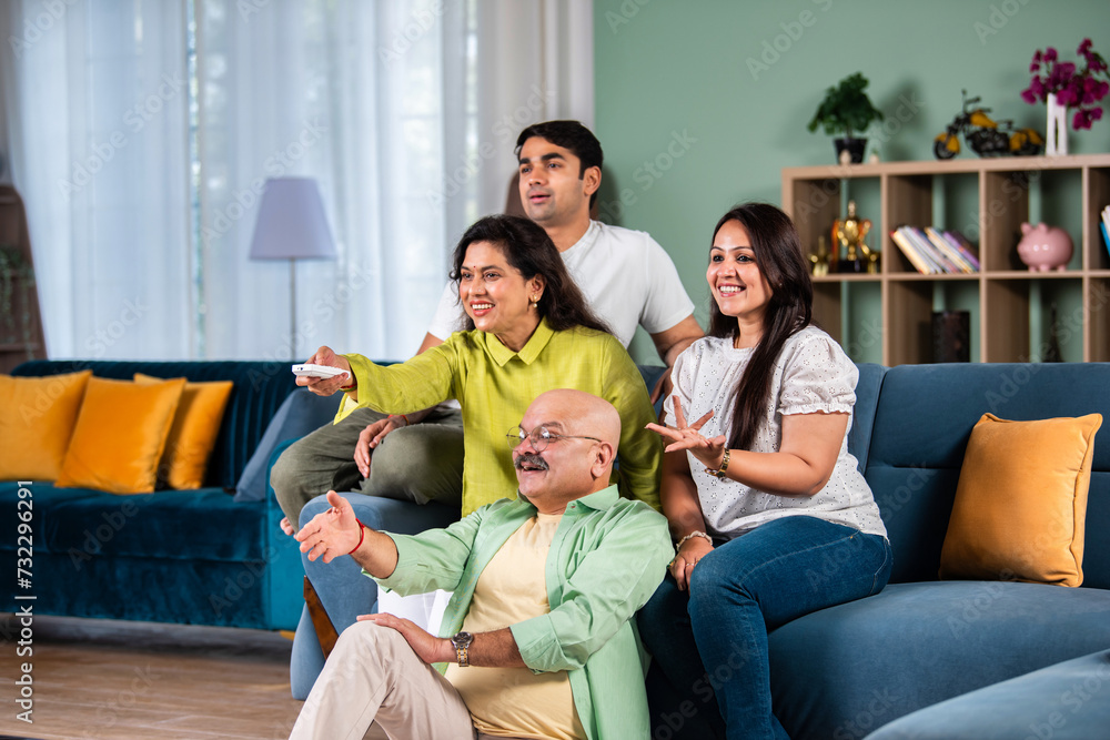 Indian family of four sitting on couch watching TV, operating with remote control Indian family of four sitting on couch watching TV, operating with remote control
