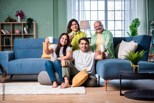 Cheerful Indian family enjoying tea or coffee together, looking at the camera