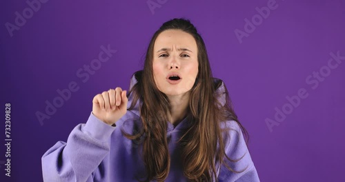 Attractive brunette woman isolated on purple background. Curious, suspicious, woman look at camera, knocking, breathes steam on the glass, wipes. Confused female. photo