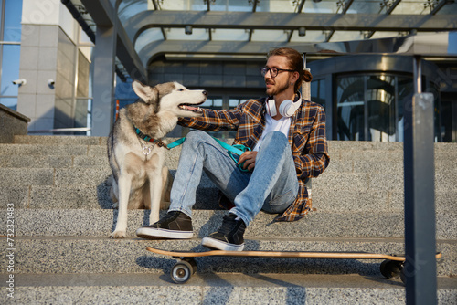 Happy hipster gay skateboarder resting and sitting with loving dog
