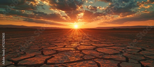 The sky is painted with vibrant colors as the sun sets over a cracked desert landscape, creating a mesmerizing dusk.