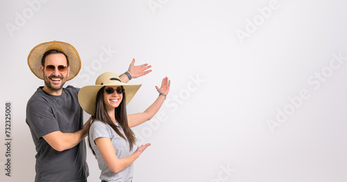 Portrait of smiling young couple wearing sunglasses and hats showing copy space on white background photo