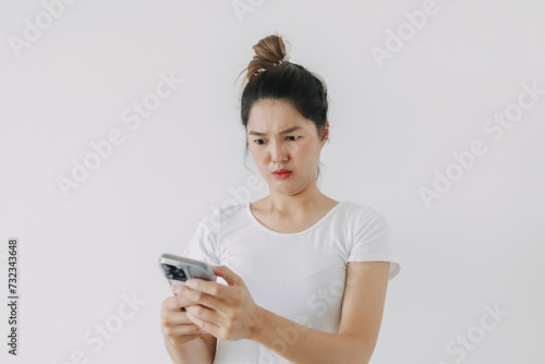 Asian Thai woman using mobile phone with funny doubt face, holding smartphone by silent suspicious, standing isolated over white background wall.