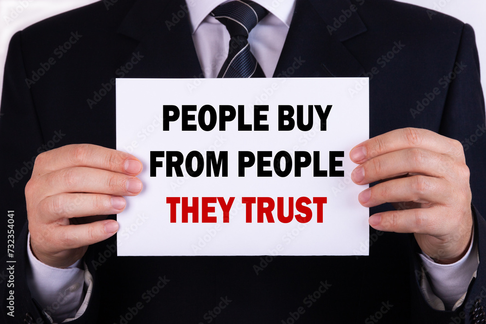 Businessman holding a card with text People Buy From People They Trust Businessman holding a card with text People Buy From People They Trust