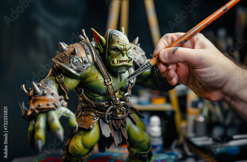 Close-up shot of a person's hand holding a paint brush, painting a large finely crafted miniature fantasy green ogre photo