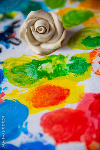 White rose on the background of a multicolored palette of paints