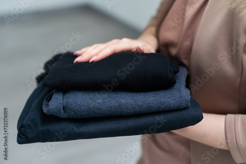 Hand holding basic t-shirts of different colors against grey background. Casual clothes for men or women  fashion concept