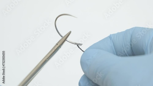 Male doctor's hands in strike gloves extend the thread into a curved surgical needle, suture material
