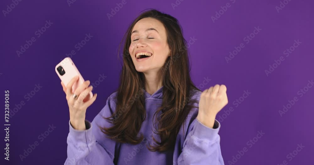Attractive brunette woman look surprised wow hold using mobile cell phone on purple background. Girl look on smartphone and doing winner gesture. Girl just found out big win news, win gesture. Attractive brunette woman look surprised wow hold using mobile cell phone on purple background. Girl look on smartphone and doing winner gesture. Girl just found out big win news, win gesture.