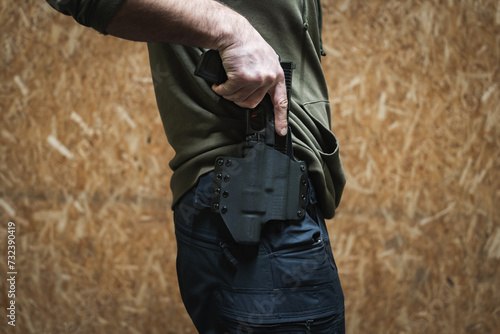 The man takes out a tactical pistol from his holster, close-up photo without a face.