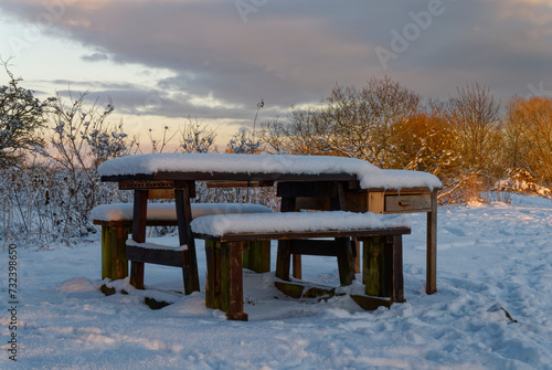 Snow covered wooden benches and Picnic Table along the River Bank in The Lurgies area of Montrose on a freezing evening in January.