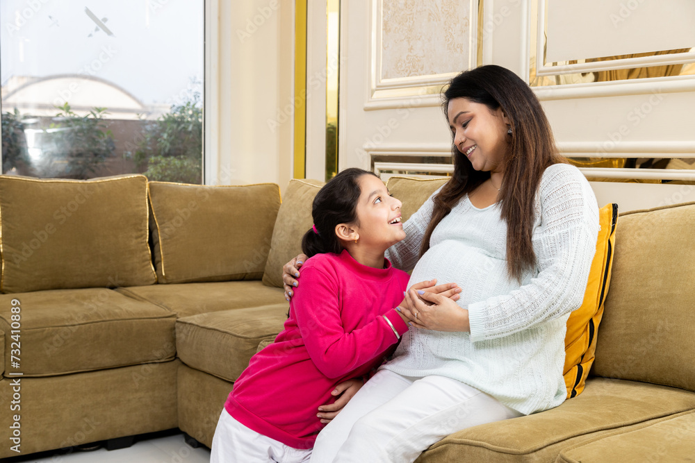Happy indian woman expecting a baby daughter touching her belly while sitting on couch. healthcare concept Happy indian woman expecting a baby daughter touching her belly while sitting on couch. healthcare concept