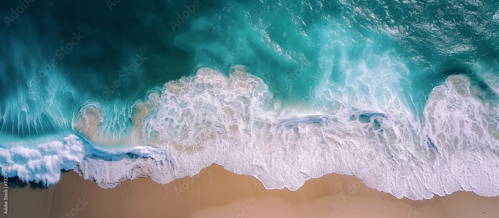 An artistic display of electric blue waves crashing on a sandy beach, witnessed from an aerial view. The sky, adorned with cumulus clouds, adds to the beauty of this meteorological phenomenon. An artistic display of electric blue waves crashing on a sandy beach, witnessed from an aerial view. The sky, adorned with cumulus clouds, adds to the beauty of this meteorological phenomenon.