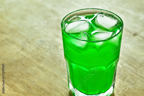 green drink. on a light wooden table there is a small transparent glass with a green drink and ice cubes, drink concept