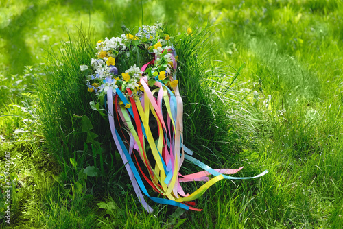 Spring flower wreath with colorful ribbons on grass in garden. floral decor. Symbol of Beltane, Wiccan Celtic Holiday beginning of summer. wheel of the year. pagan traditions, magic witch rituals