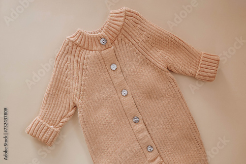 Knitted jumpsuit for a newborn on a beige background. Outerwear for toddlers for walks in autumn or spring