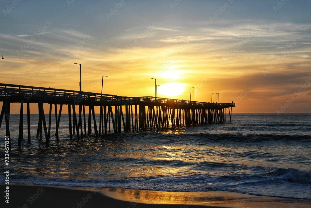 the pier extends into the ocean at sunset with clouds and bright sunlight