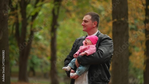 Contented father holds sleeping child in quiet park with autumn leaves in background. Concept of parental love and family.