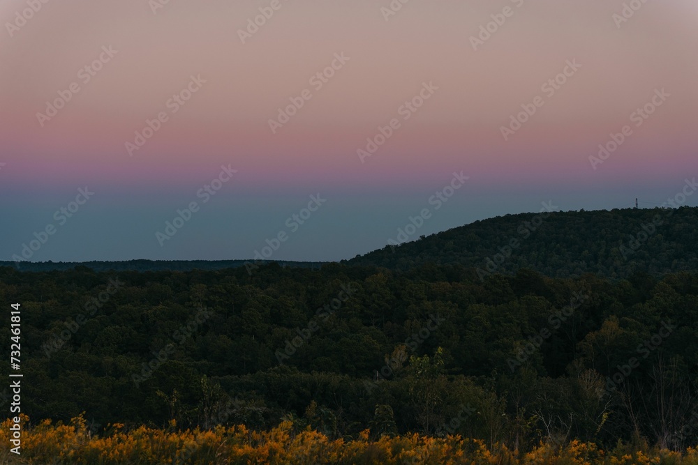 Scenic view of a mountain range covered with green forest at sunset