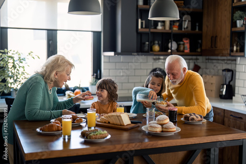 Grandchildren having breakfast with grandparents in home atmosphere.