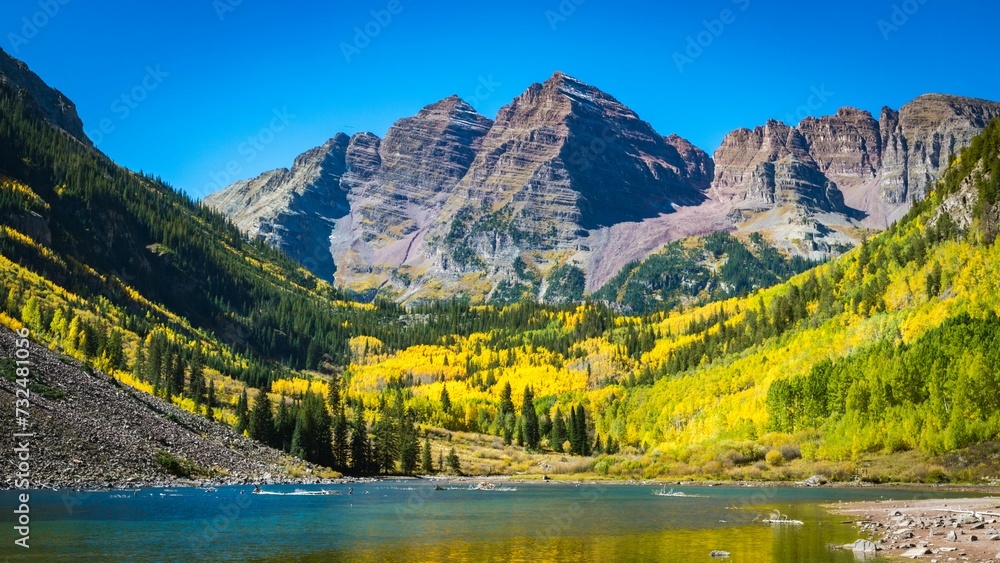Fototapeta premium Tranquil lake surrounded by majestic mountains under a bright sky, with trees in the foreground