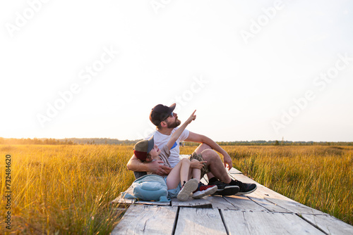 Quadro su tela Father and son sitting on wooden boardwalk through swamp