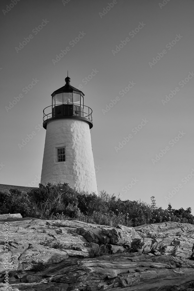 Grayscale of the Pemakid Point Lighthouse illuminated against a backdrop of a rocky shore