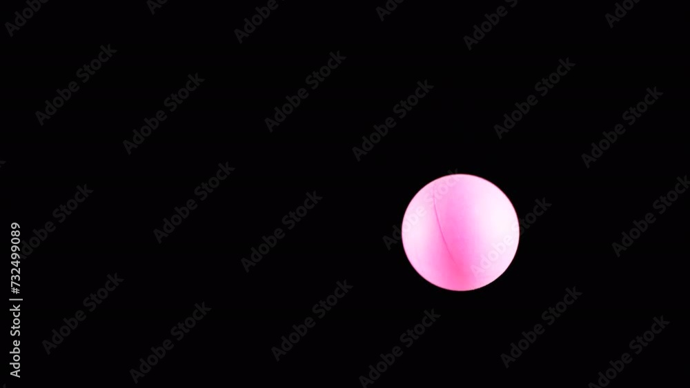 Pink Small Tennis Ball Spinning in Copy Space on Black Background. Abstract. Side view. Plastic sphere or ball balances in the air flow. levitation. Selective focus. One hovering, flying ball. Light. Pink Small Tennis Ball Spinning in Copy Space on Black Background. Abstract. Side view. Plastic sphere or ball balances in the air flow. levitation. Selective focus. One hovering, flying ball. Light.