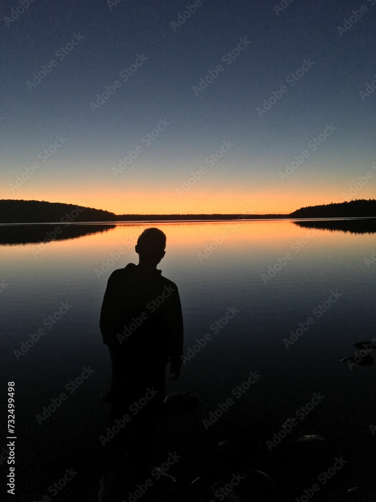 Man near the edge of a tranquil lake, overlooking the horizon at sunset