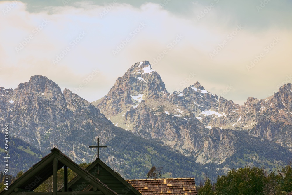 a cross is seen atop an older wooden church in front of the mountains