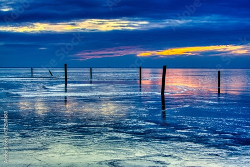 Scenic view of wooden pillars at the shore of a frozen lake at sunset