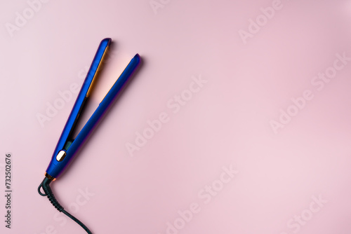 Purple hair straightener on pink background. Copy space