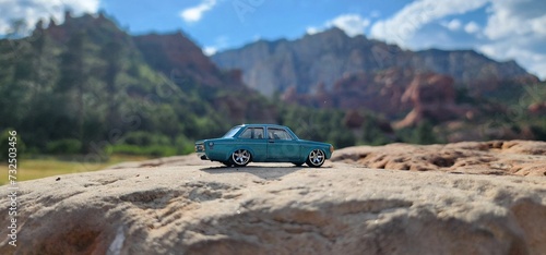Miniature toy car perched atop a large rock, with majestic mountain peaks in the distant background photo