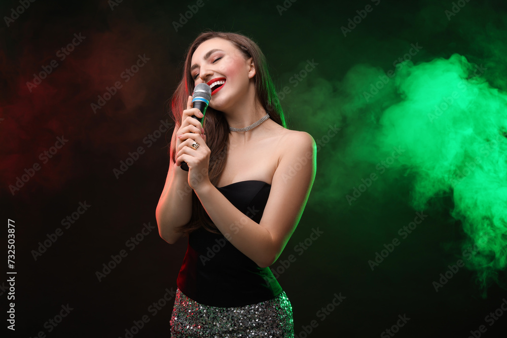 Beautiful woman with microphone singing in color lights on dark background Beautiful woman with microphone singing in color lights on dark background