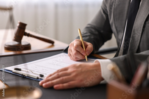 Notary writing notes at wooden table in office, closeup