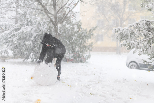 a girl is playing with snow on the street, it is snowing, a blizzard and frost on a winter day