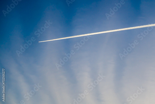 White trail of flying plane on blue sky clouds background