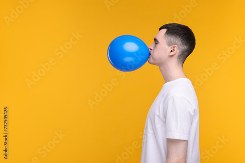 Young man inflating light blue balloon on yellow background. Space for text photo