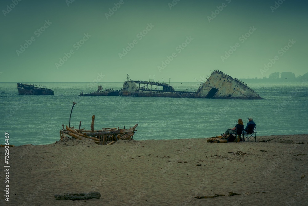 two people on the beach siting next to a sunken ship: California, Aptos