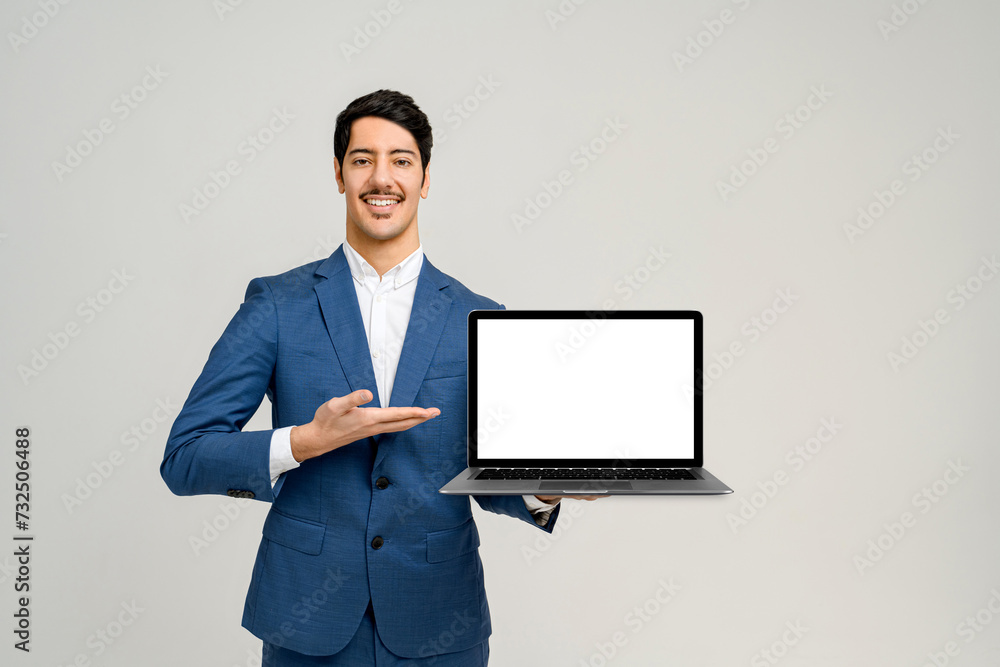Man in a smart blue suit stands against a clean background, holding a laptop with a blank screen towards the camera, the perfect template for graphic designers to superimpose an application or website - obrazy, fototapety, plakaty 