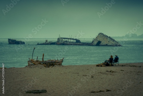 two people on the beach siting next to a sunken ship: California, Aptos photo