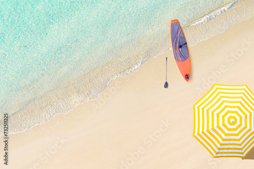 Top view of woman in bikini and hat lying near umbrella and sunbathes on tropical Seychelles sea sand beach with SUP board for surfing. Aerial, drone view