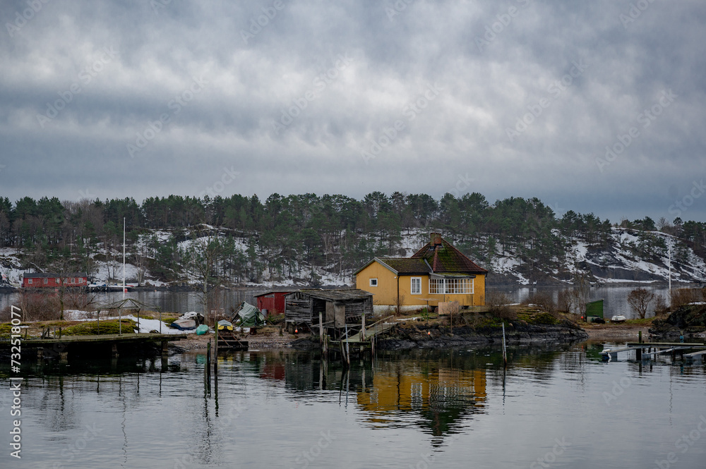 A wooden Norwegian cottage on the shore of the Oslo fjord on a winter day. Yellow house on the shore