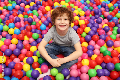 Happy little boy sitting on colorful balls in ball pit