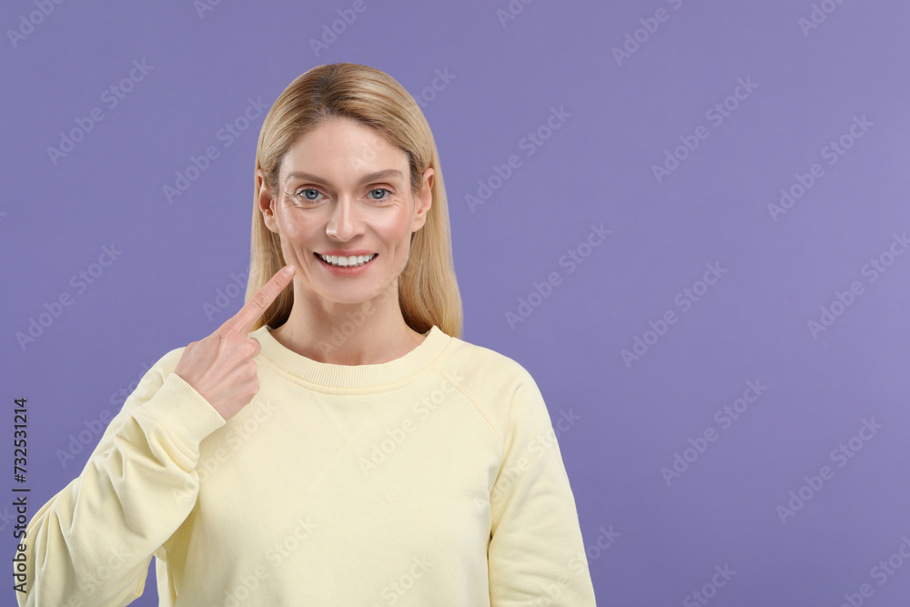 Woman showing her clean teeth and smiling on violet background, space for text Woman showing her clean teeth and smiling on violet background, space for text