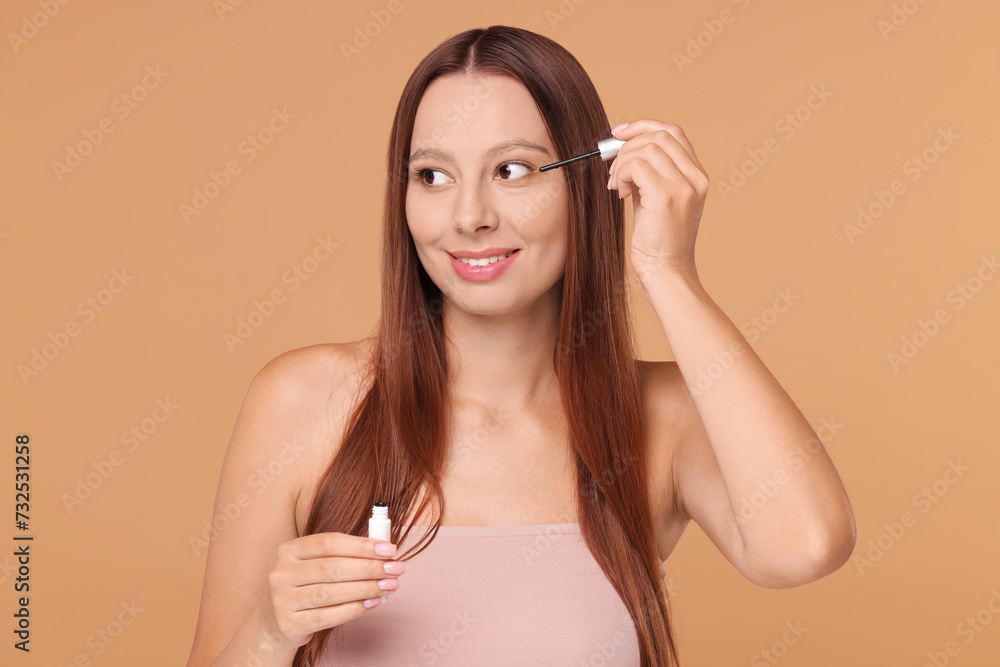 Beautiful woman applying serum onto eyelashes on beige background Beautiful woman applying serum onto eyelashes on beige background