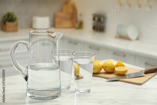 Jug, glasses with clear water and lemons on white table in kitchen © New Africa