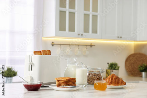 Making toasts for breakfast. Appliance, crunchy bread, honey, jam, milk and croissant on white marble table in kitchen